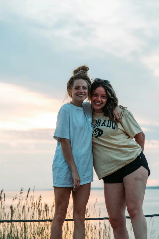 two girls hugging in front of the water with the sky in the background