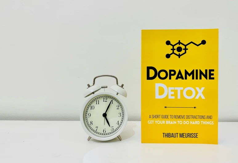 a white clock next to a yellow book with the word dopamina detox