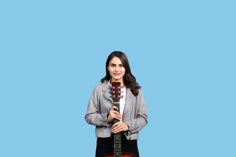 an indian woman stands with her guitar against a blue background