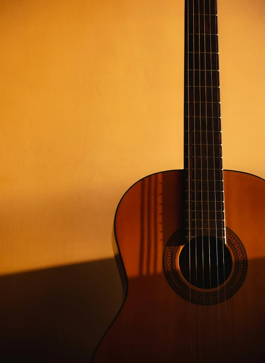 a brown acoustic guitar hanging up against a yellow wall