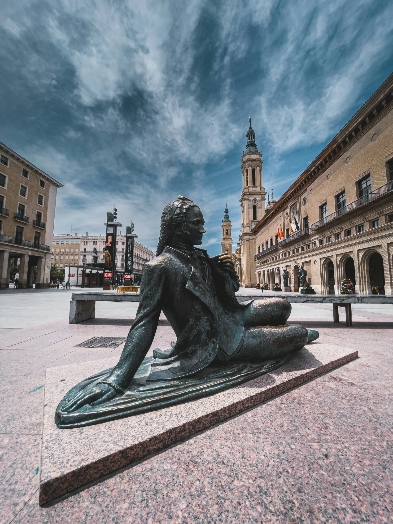 a statue sits on the ground with people walking around in the background