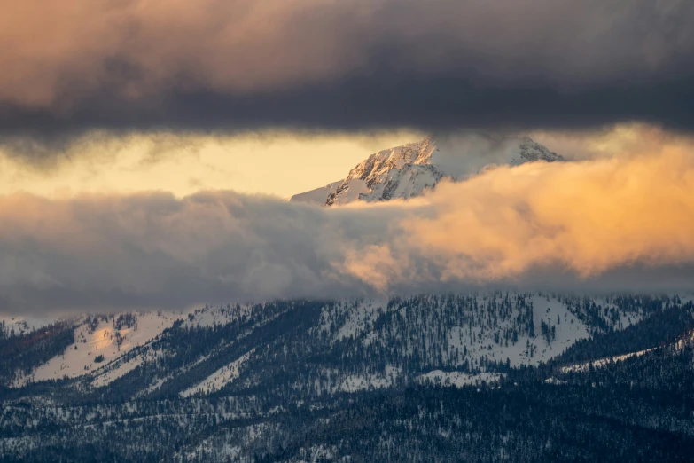 mountain peaks covered in snow and clouds with orange lights coming on