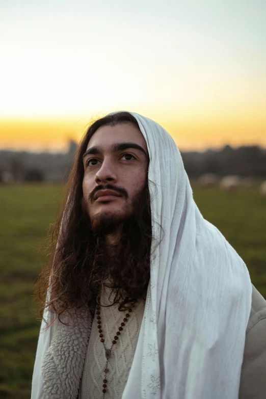 a man with a beard and white shawl stands in the field