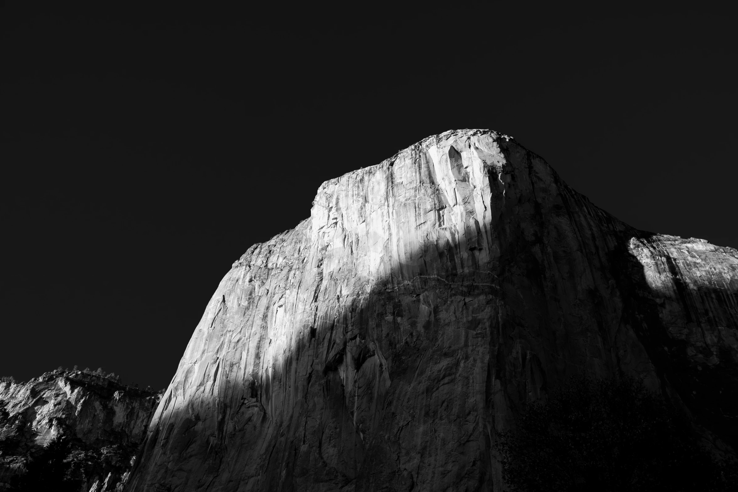 black and white image of the side of a mountain with sun shining on it