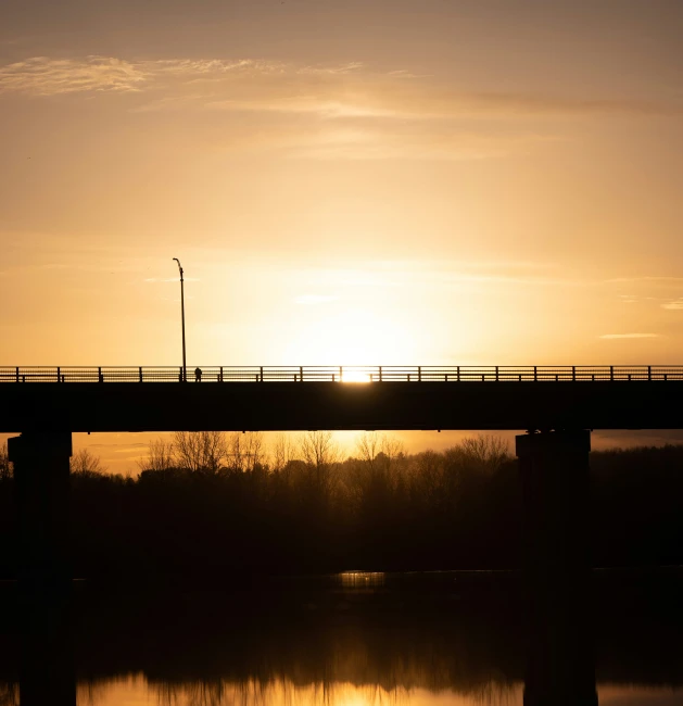 a bridge with the sun setting behind it