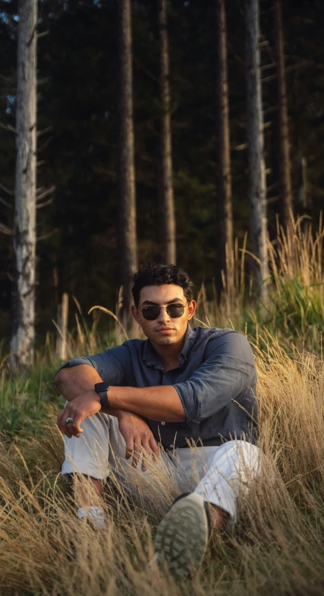 a man sitting in some grass with sunglasses on