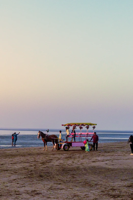 a pink and yellow truck with some people around it on the beach