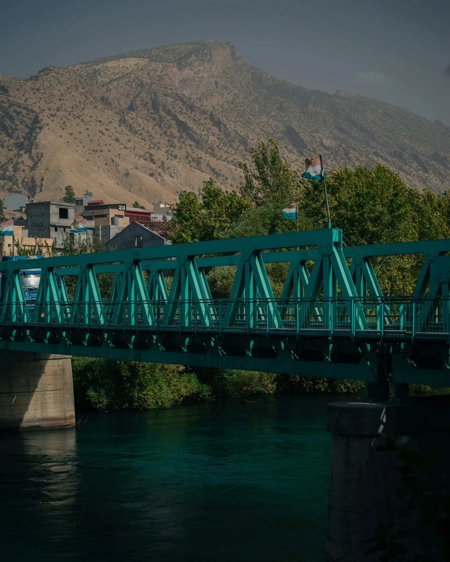 a green bridge over a river surrounded by mountains