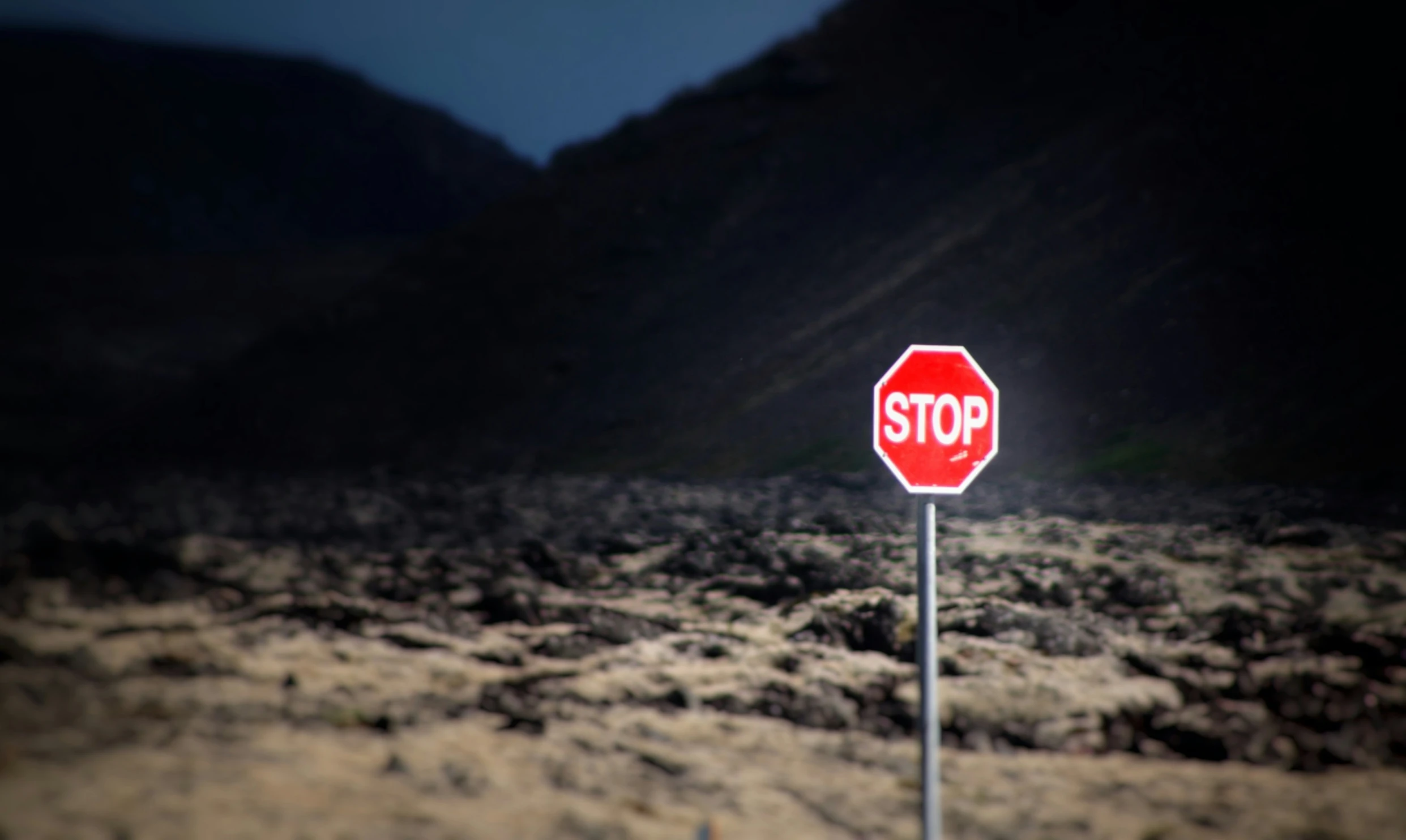 the red stop sign is posted in a rocky field