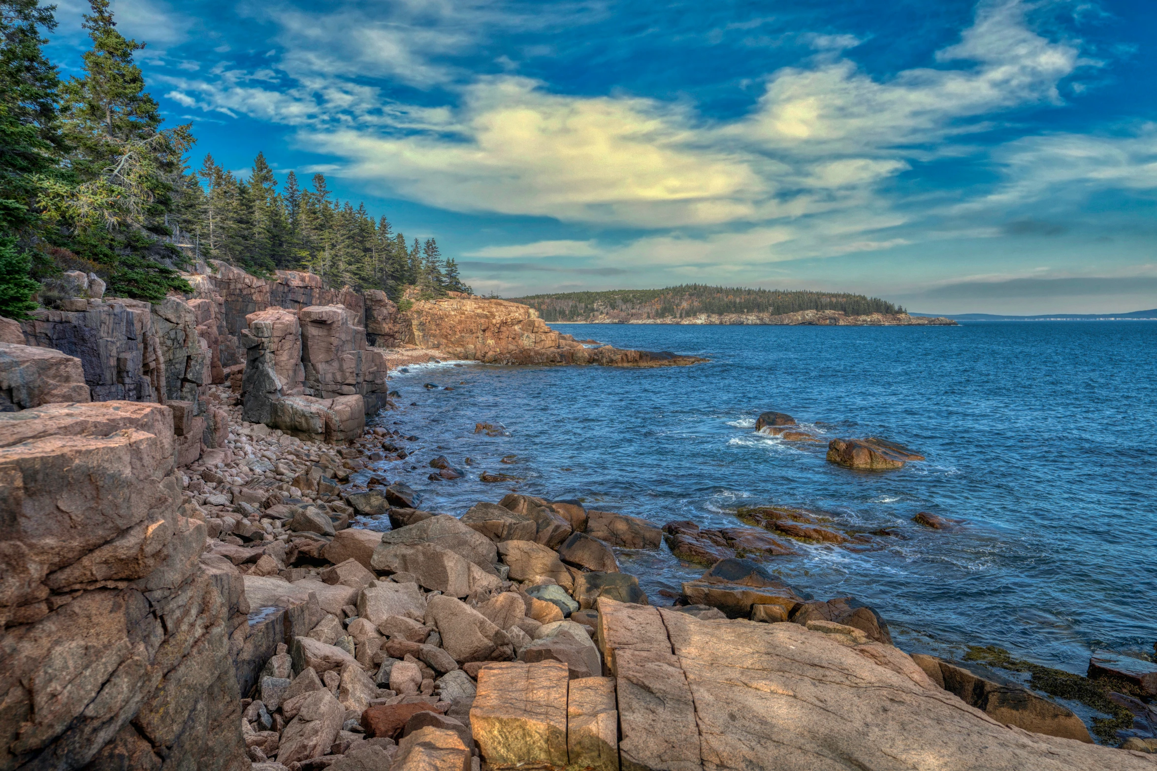 a rocky beach with blue sky and clouds over it