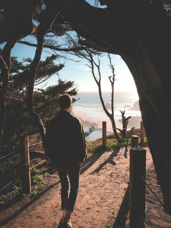 man standing in front of fence on road overlooking beach