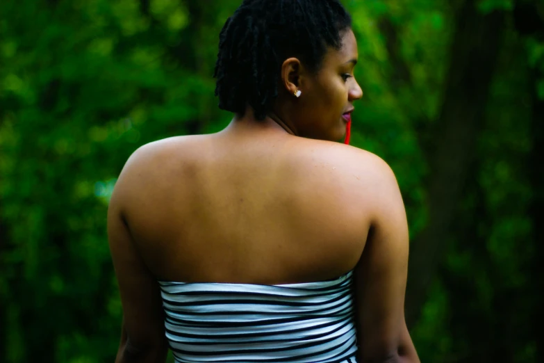 a woman in a striped dress looks around in front of trees