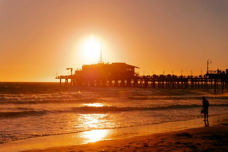 the sun is setting over a pier on a beach