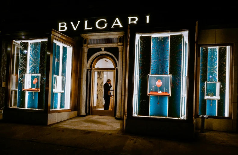 a man stands outside of a bulgari shop at night