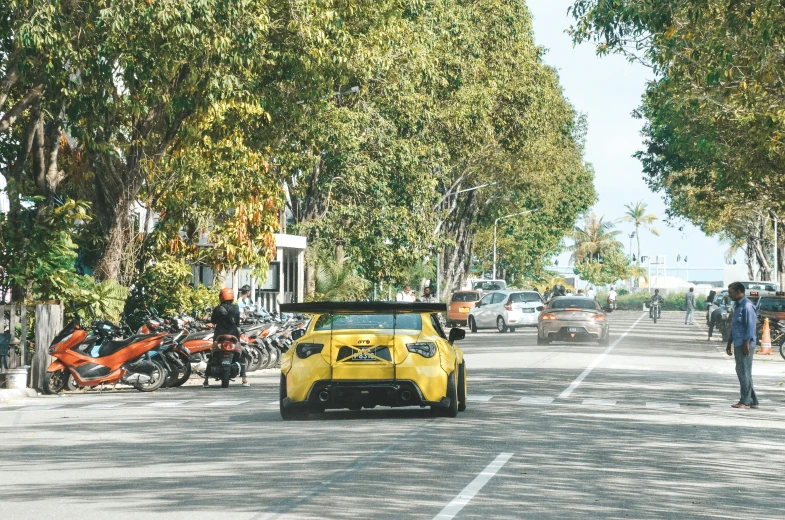 yellow car driving on the street next to people and motorcycles