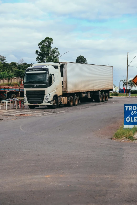 a tractor trailer driving down a street with a sign in front of it