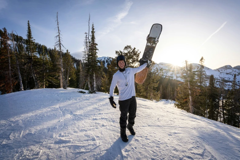 a man holding up his snowboard on top of a mountain