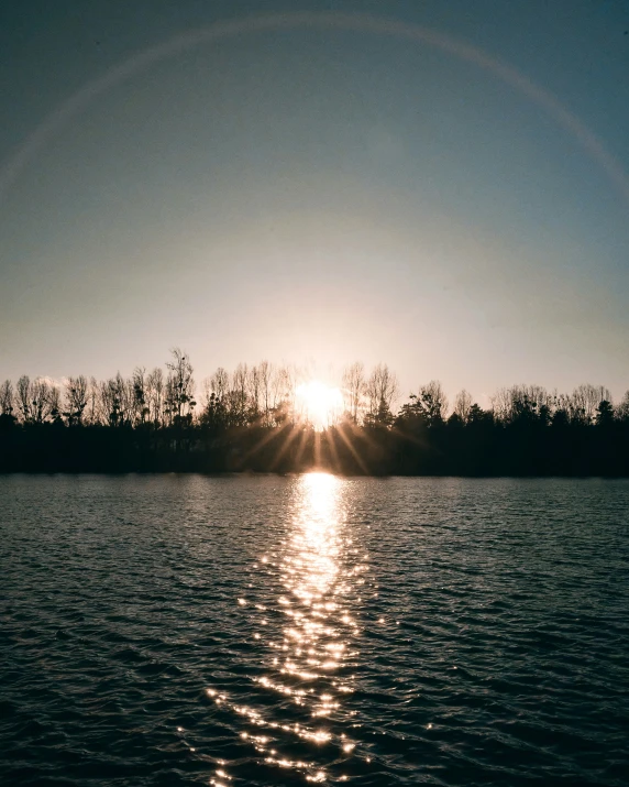the sun shining through the dark blue sky over a lake