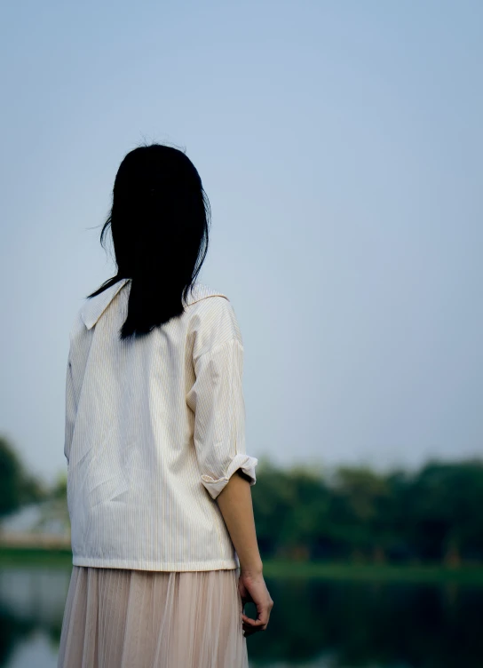 an asian woman wearing a striped shirt and a skirt looking across a river