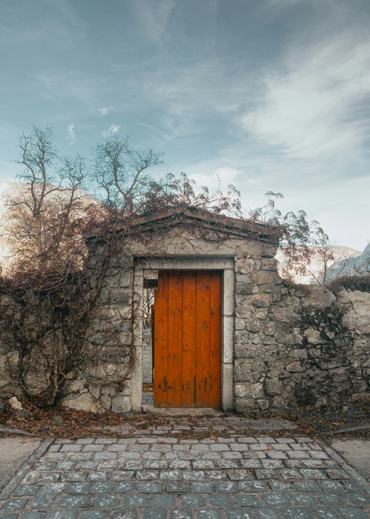 a brick building with an orange door surrounded by a stone fence