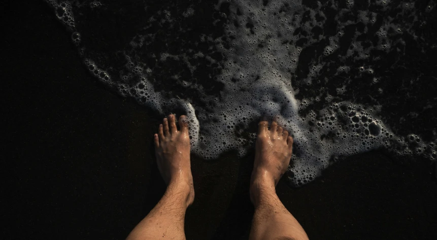 legs in the sand, water coming out of it, and black sand at the beach