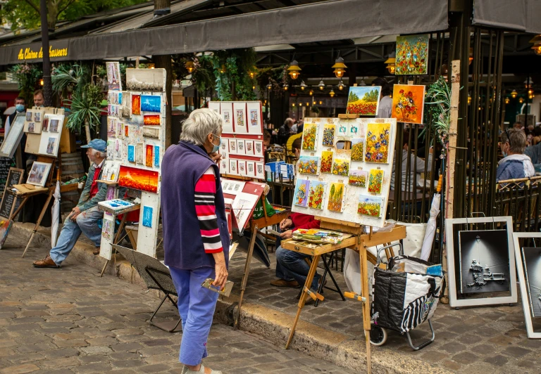 a woman looking at paintings for sale on a street