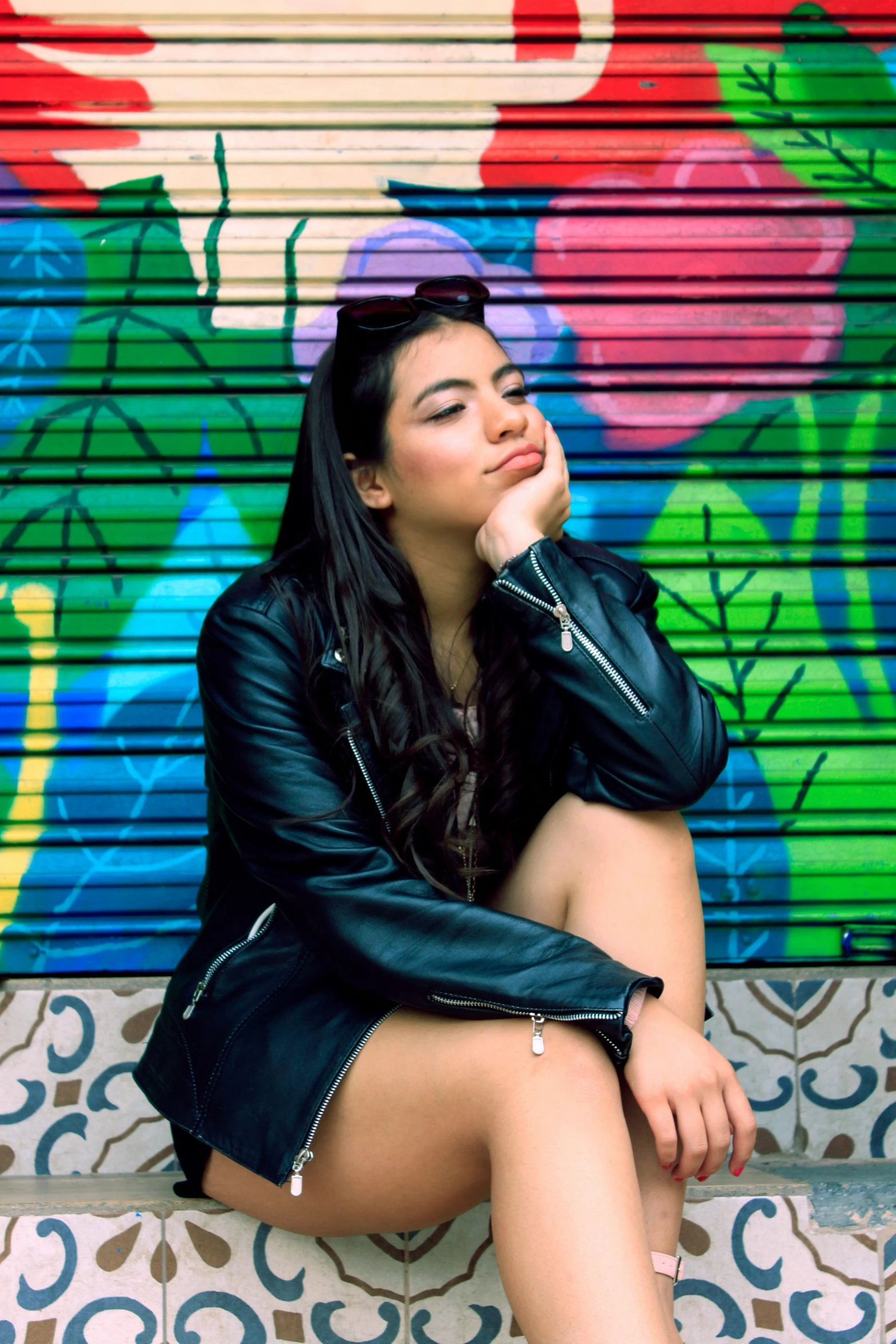 woman in short skirt and leather jacket sitting down on a bench