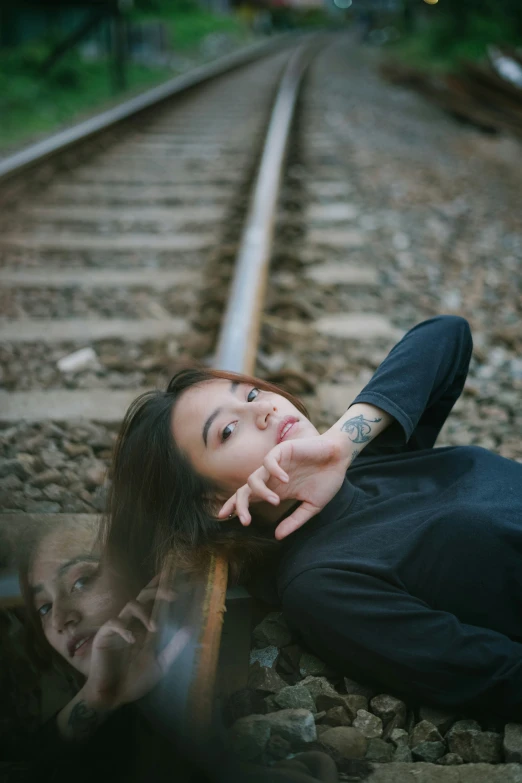 woman laying on railroad tracks with hand pointing at camera