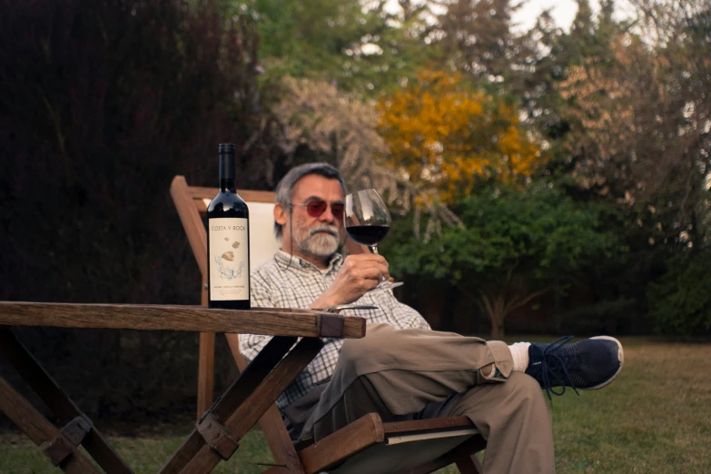 a man sitting in a chair holding up a wine glass and bottle