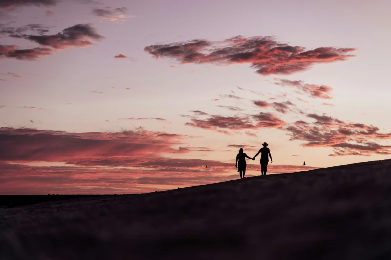 two people stand on top of a hill and hold hands