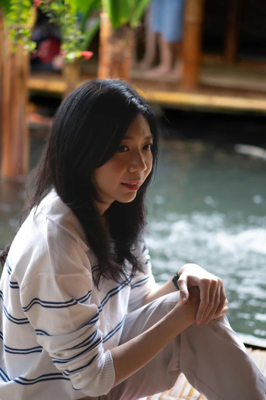 a woman sitting by the water with her legs crossed