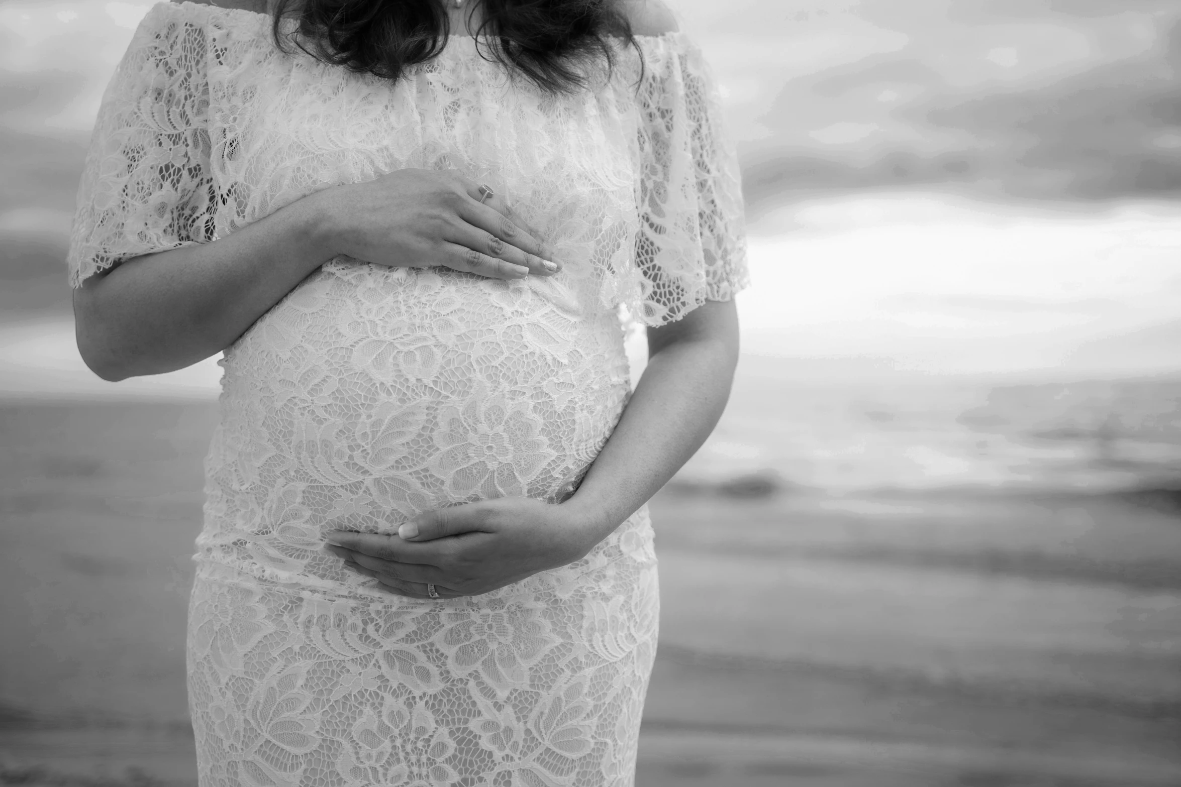 the pregnant woman poses on the beach for a black and white po