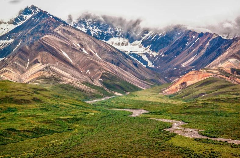 a mountain landscape with green grass and a river