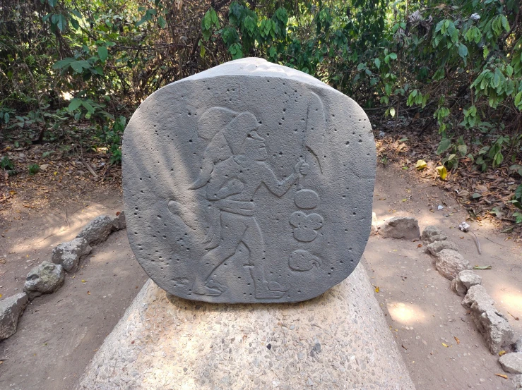 a large boulder with intricate carved decorations sits in front of green trees