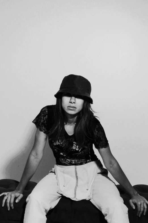 a woman sitting on a couch wearing white pants and a hat