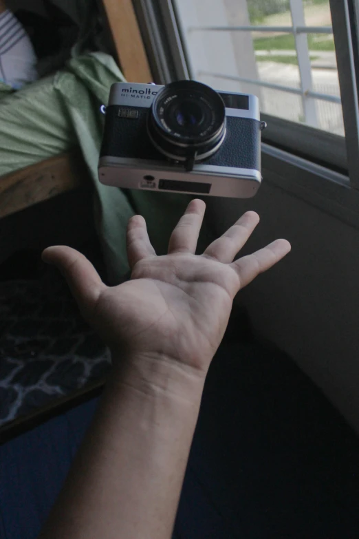 a hand is holding a camera in front of a window