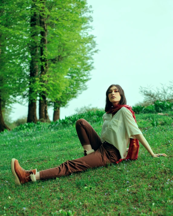 woman with brown hair wearing a white blouse sitting on the grass