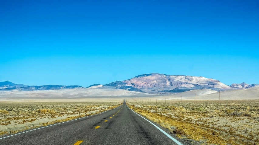 the road in the desert is leading towards the mountains