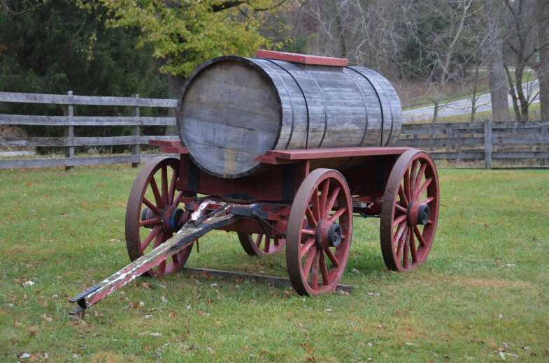 a cart with a large wooden barrel sitting in the grass