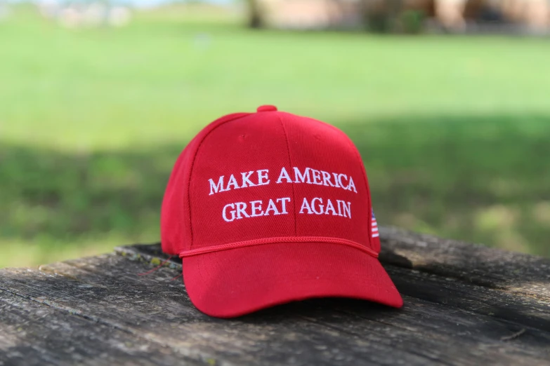 red baseball cap sitting on wooden table with grass behind it