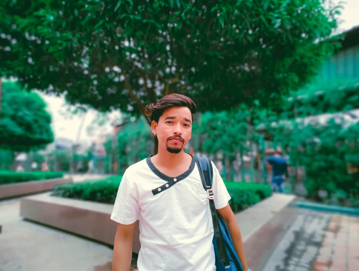 man standing in the park holding a bag, wearing a backpack