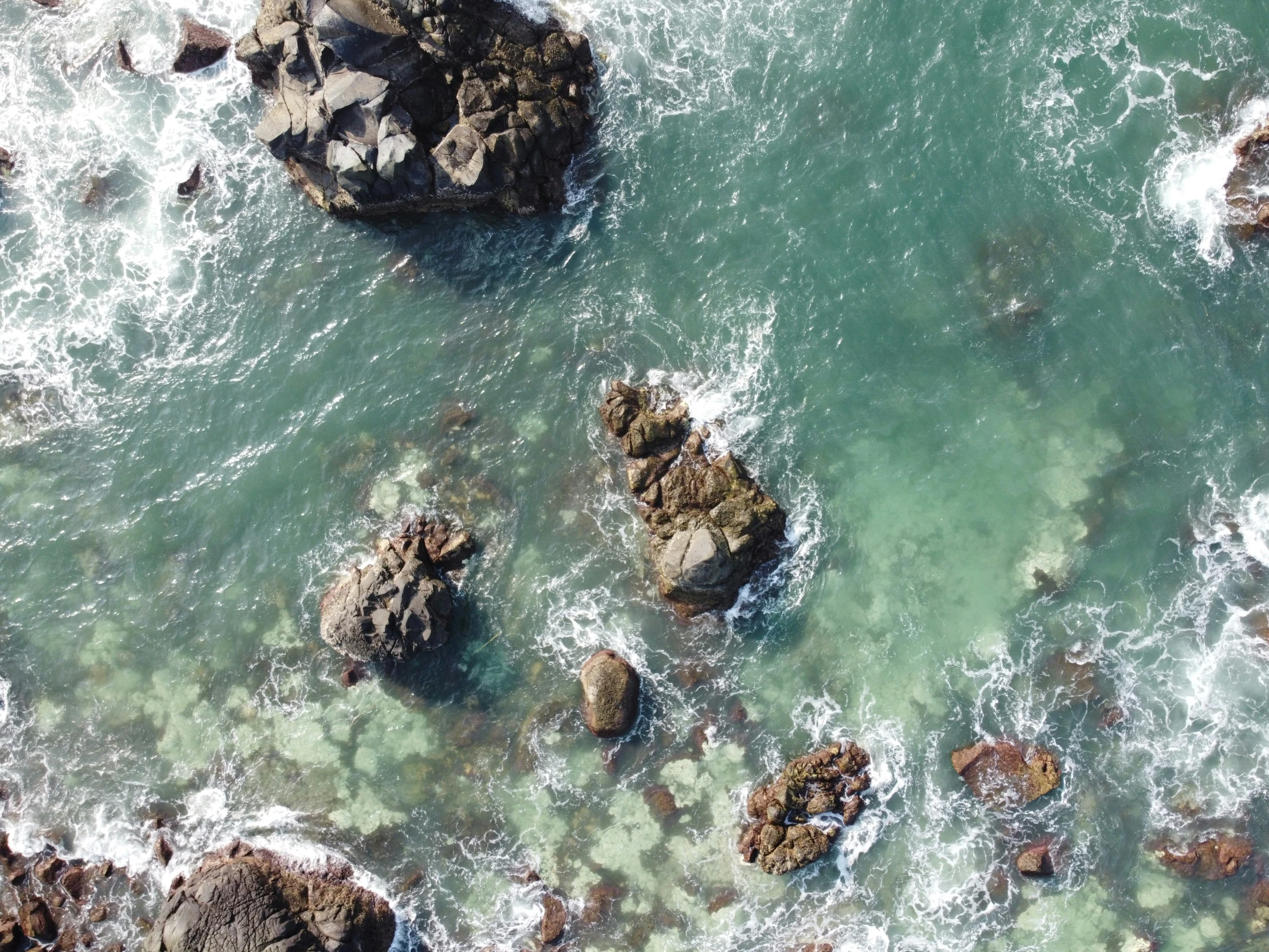 sea waves crashing in between rocky, blue ocean waters