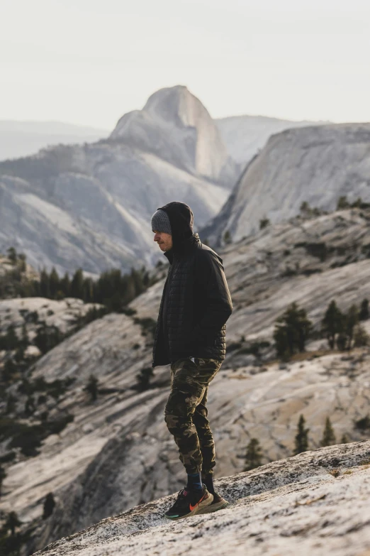 the man stands on the edge of a mountain overlooking some mountains