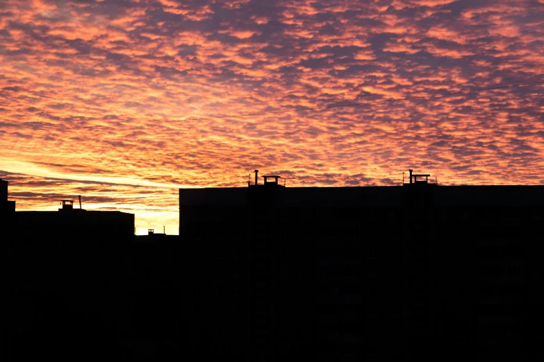 red clouds are rising over two buildings at sunset