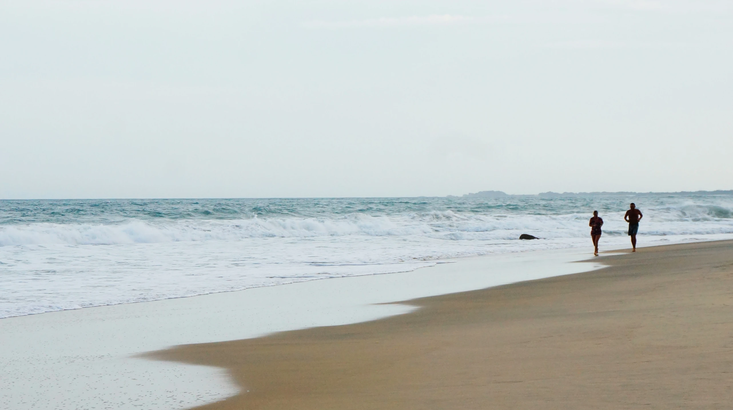 two people standing on the beach while looking at the waves