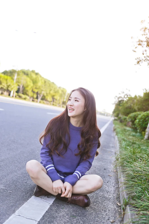 a beautiful young woman sitting on the side of a road