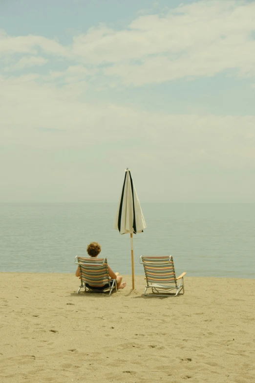 a man sits alone on the beach under an umbrella