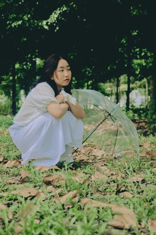 a woman kneeling down holding an umbrella in the grass