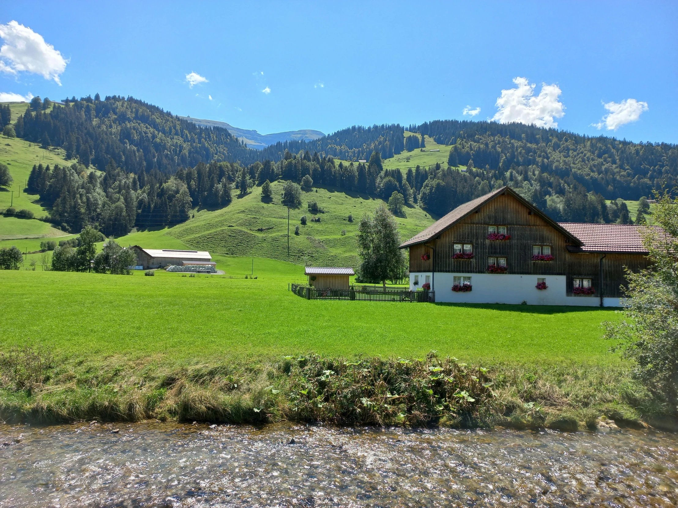 a large green pasture with two small barns in the background