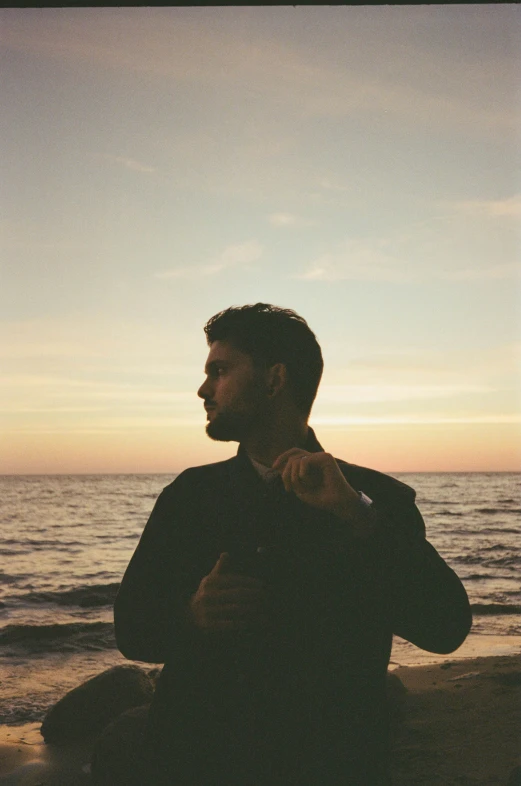 a man sitting on the beach next to a body of water